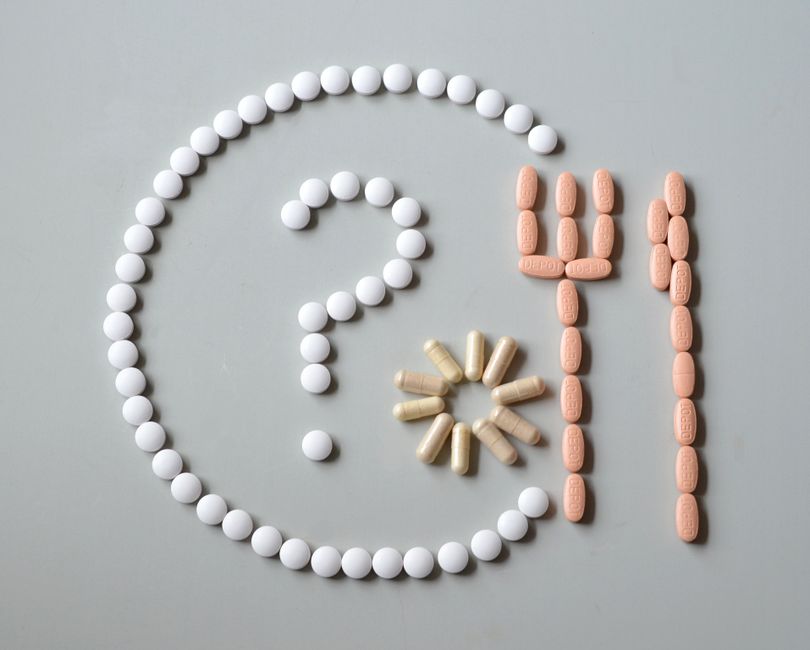 Artistic layout of various pills forming a question mark with fork and sun.